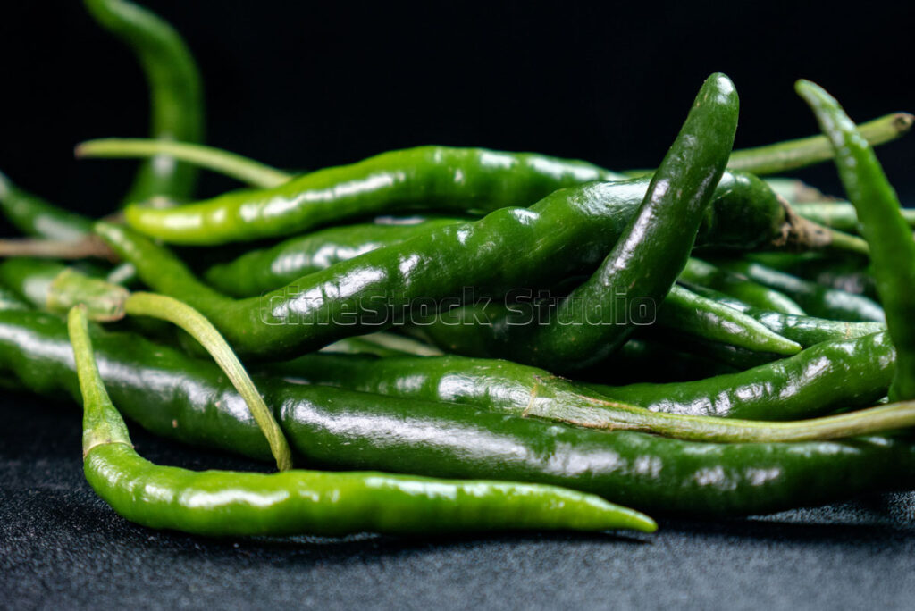 Close up of fresh green chili peppers on a dark studio background