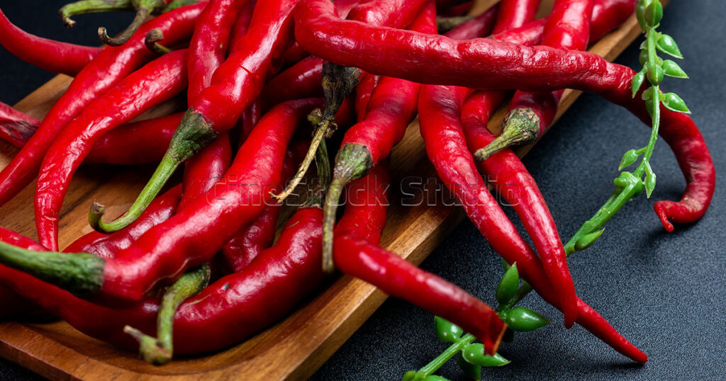 Pile of freshly harvested long red chili peppers on a wooden tray