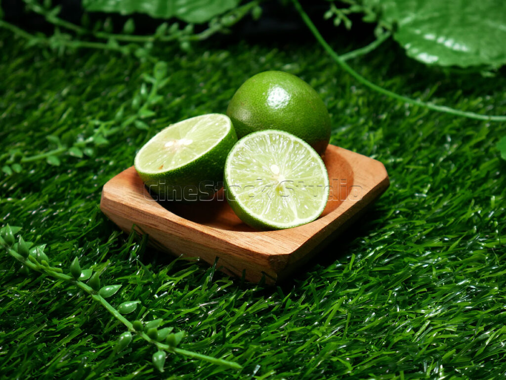Two halves of a juicy citrus fruit placed in a wooden bowl, surrounded by green foliage and grass.
