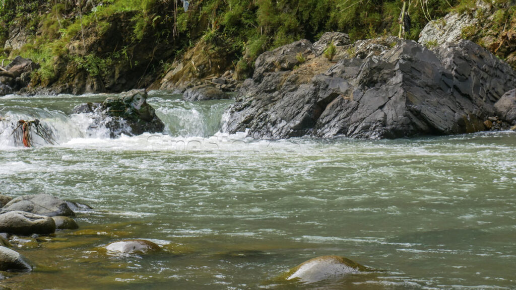 Clear river water, flowing rapidly through small rapids of large and small rocks