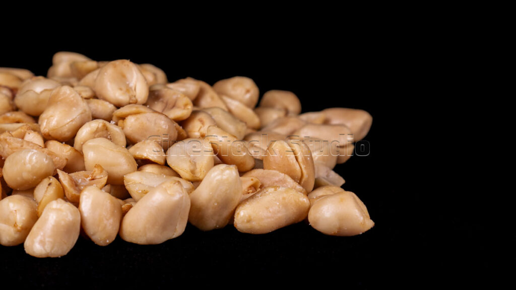 Roasted peeled peanuts scattered on dark surface.