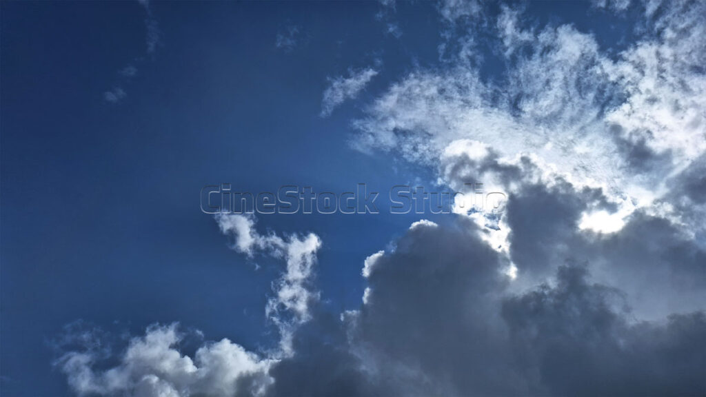 Sunlight emerging from behind dark clouds in the blue sky.