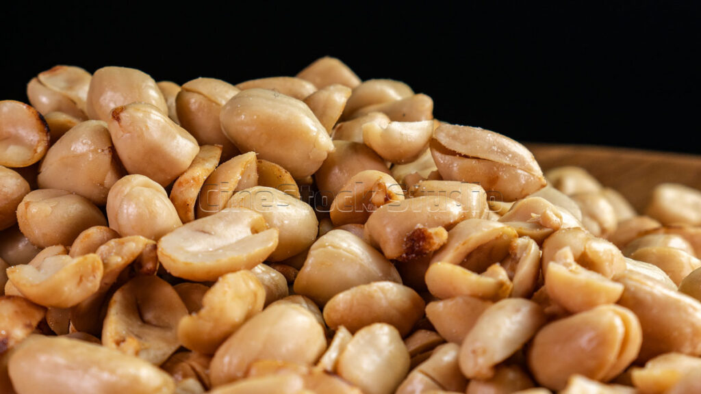 Close-up of a pile of roasted peanuts in a wooden plate.