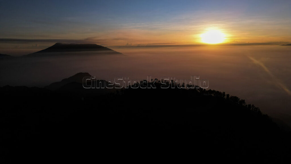 Aerial view of sunrise over mountains covered in a sea of thick fog.