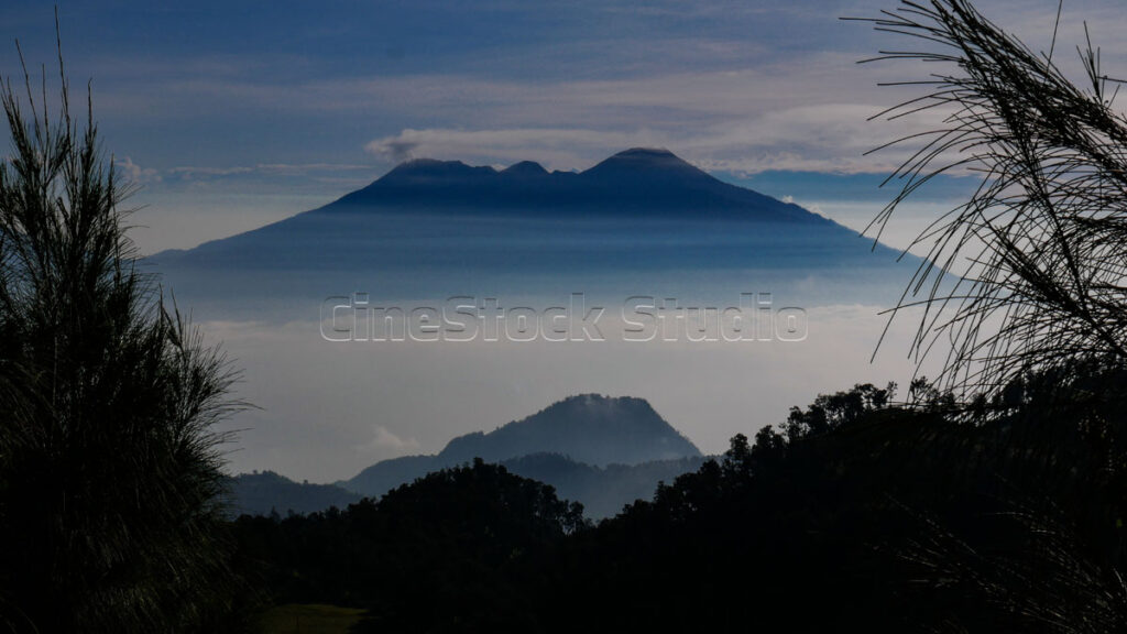 Panoramic silhouette of Mount Arjuno and Welirang with their peaks covered in thin mist.
