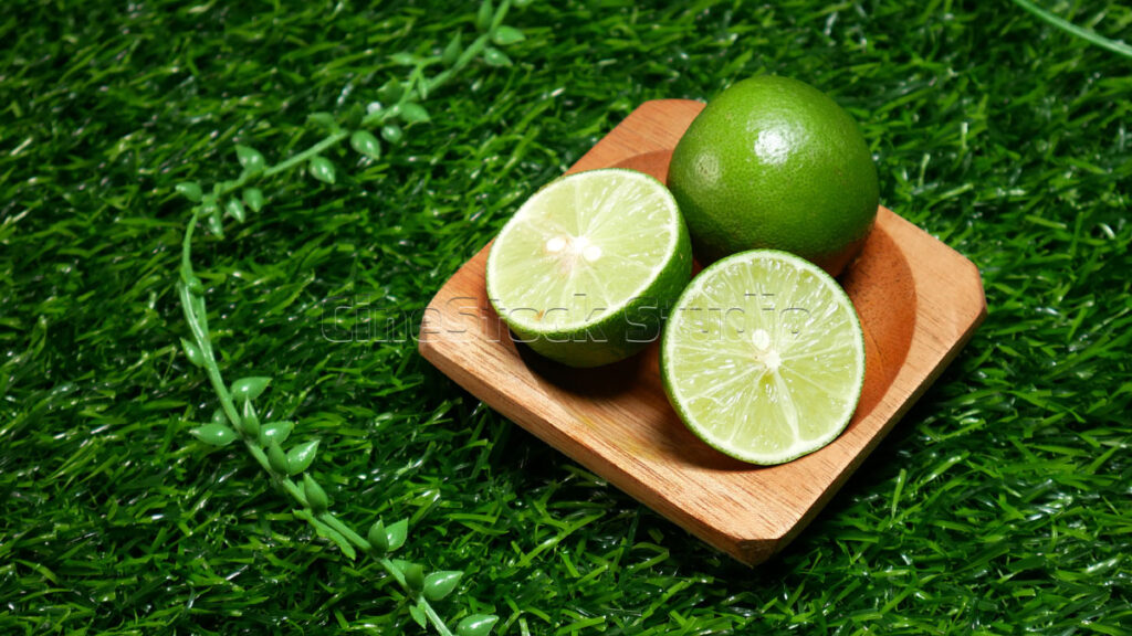 A close-up shot of sliced lime showing the internal pulp texture on a wooden saucer over artificial turf.