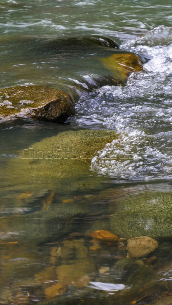 Clear river water flows over colorful and mossy rocks,