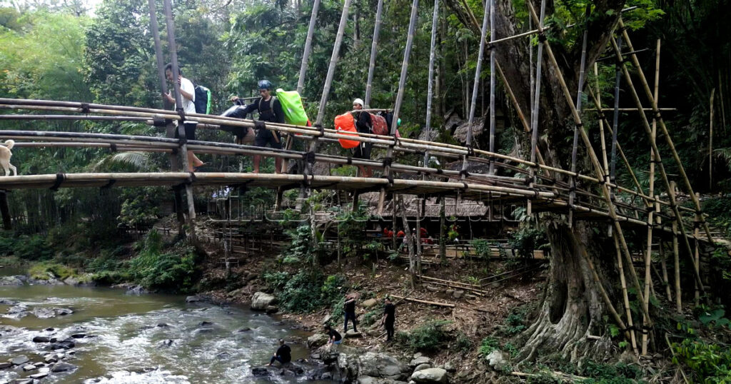 Baduy locals carrying backpacks and supplies for tourists across the Gajeboh Bamboo Bridge.