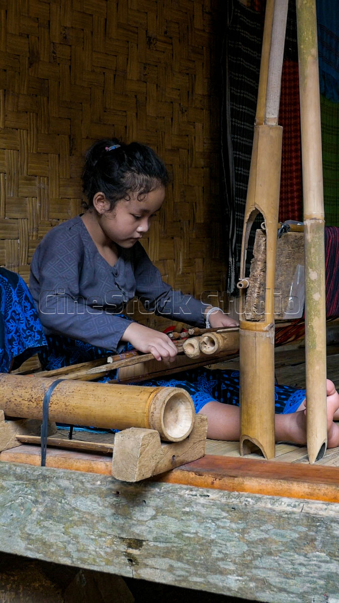 A young Baduy woman focused on operating a bamboo weaving loom