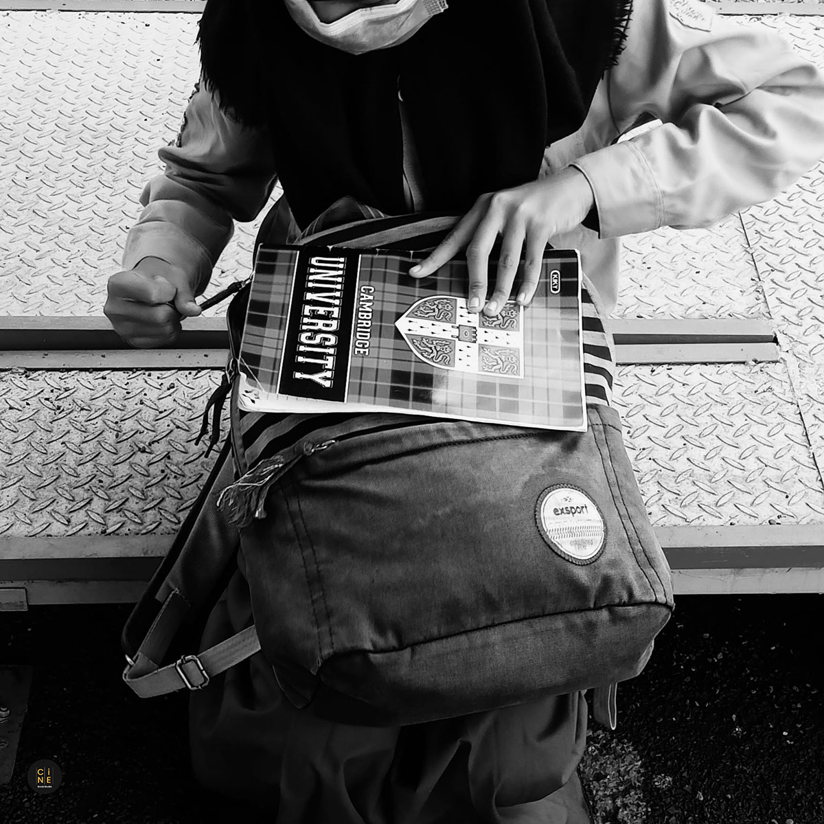 A close-up shot of a student's hands holding a book titled university on top of her school bag.