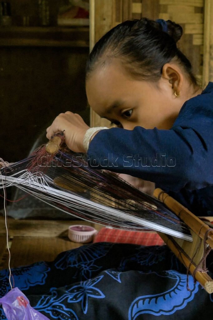 A young Baduy girl looking down with deep concentration at her weaving threads