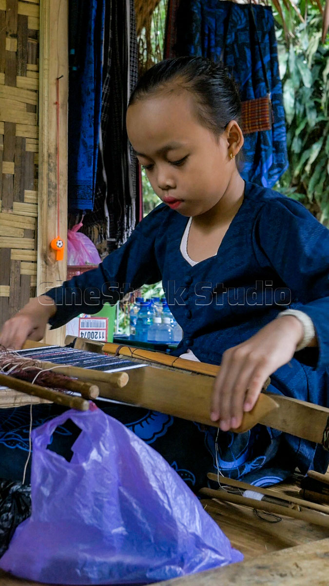 A young Baduy girl focused on her small-scale weaving loom