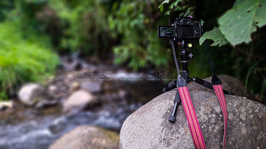 A back view of the Lumix G85 camera with a red patterned strap resting securely on top of a large river boulder.