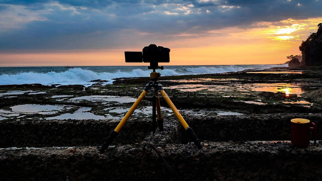 Featured image of a Lumix G85 camera on a yellow tripod capturing a dramatic golden sunset on a rocky beach.