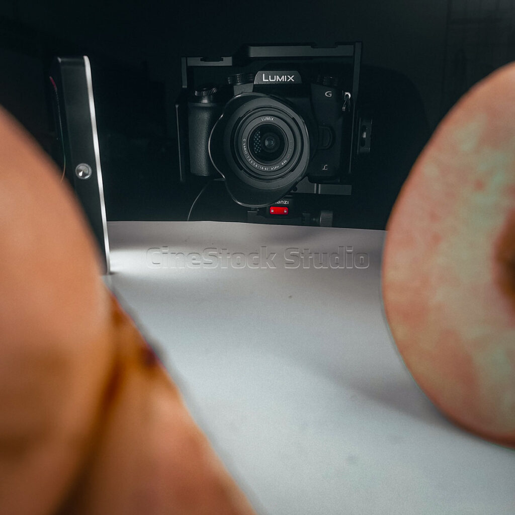 Extreme close-up perspective from behind two pear slices looking straight toward a Lumix G85 lens in a dark studio.