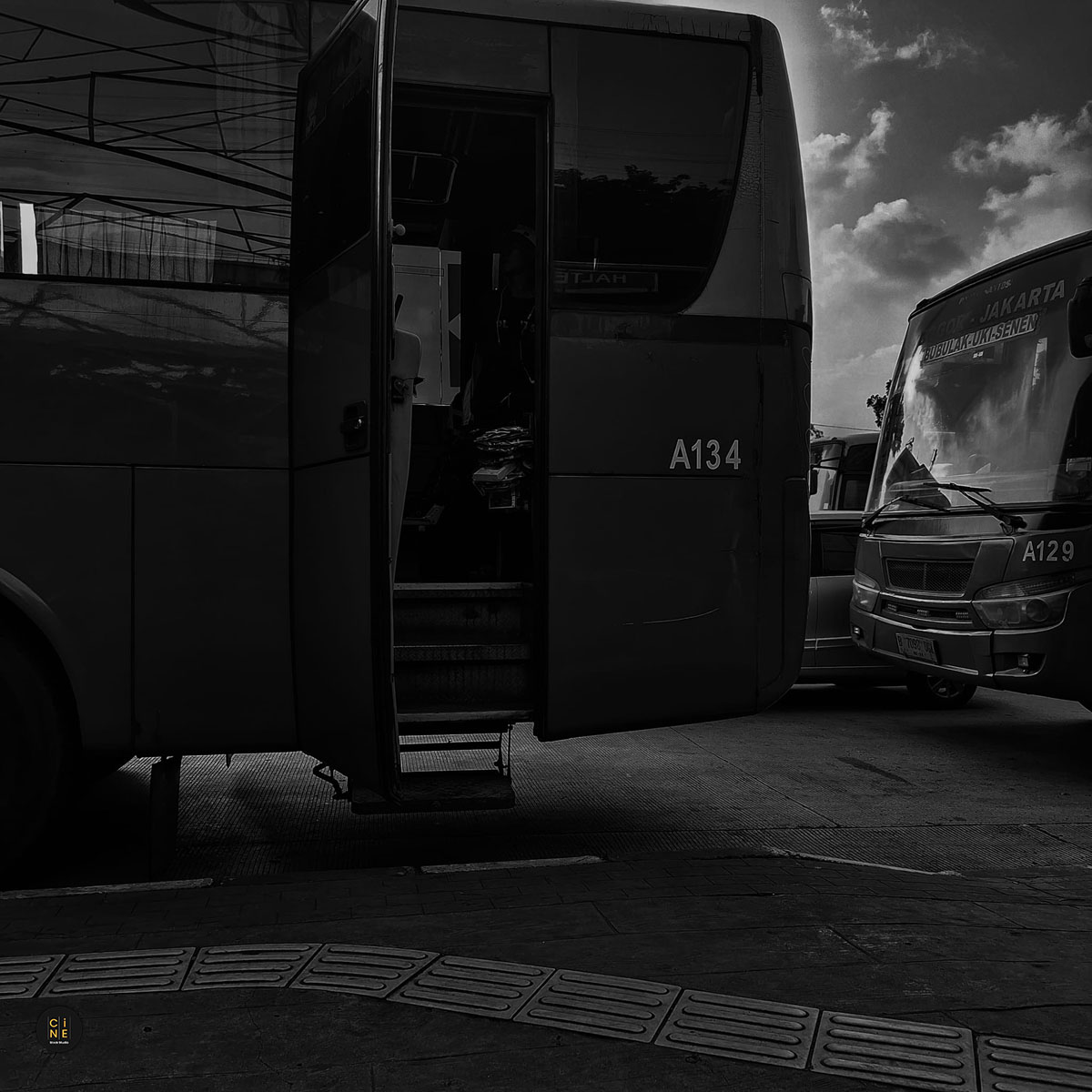 A wide horizontal monochrome frame of a large city bus parked with its passenger door wide open, revealing the dark interior.