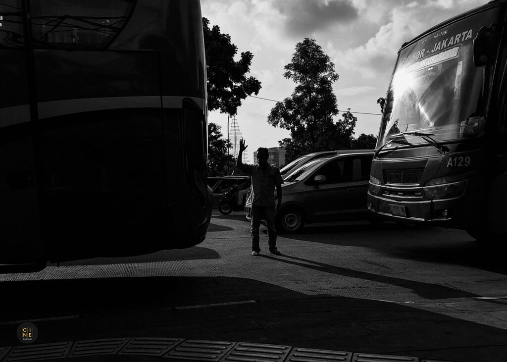A low-angle black and white shot framing a silhouette of a person standing between two large parked city buses.