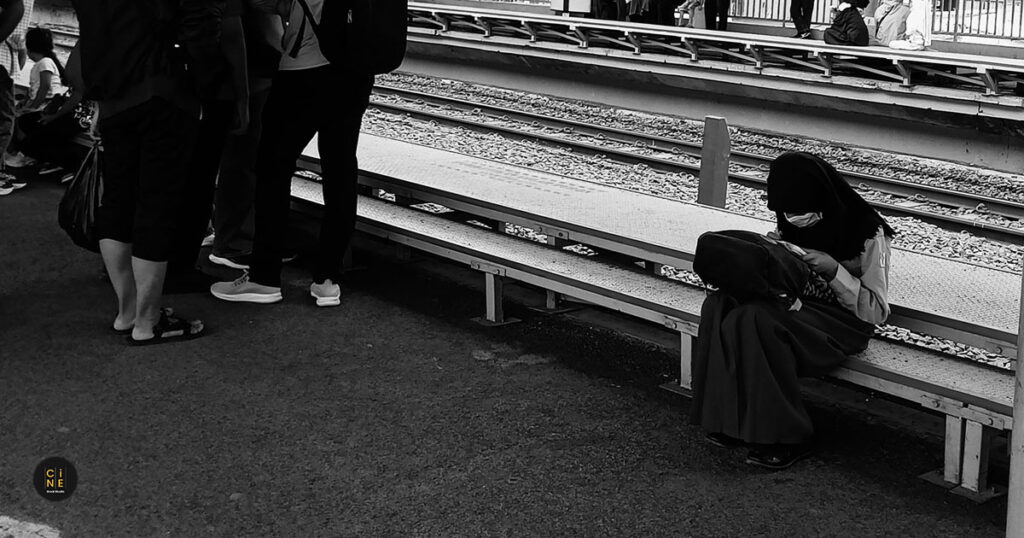 Featured image of a student doing her schoolwork on tracks while sitting on a station bench during early morning.