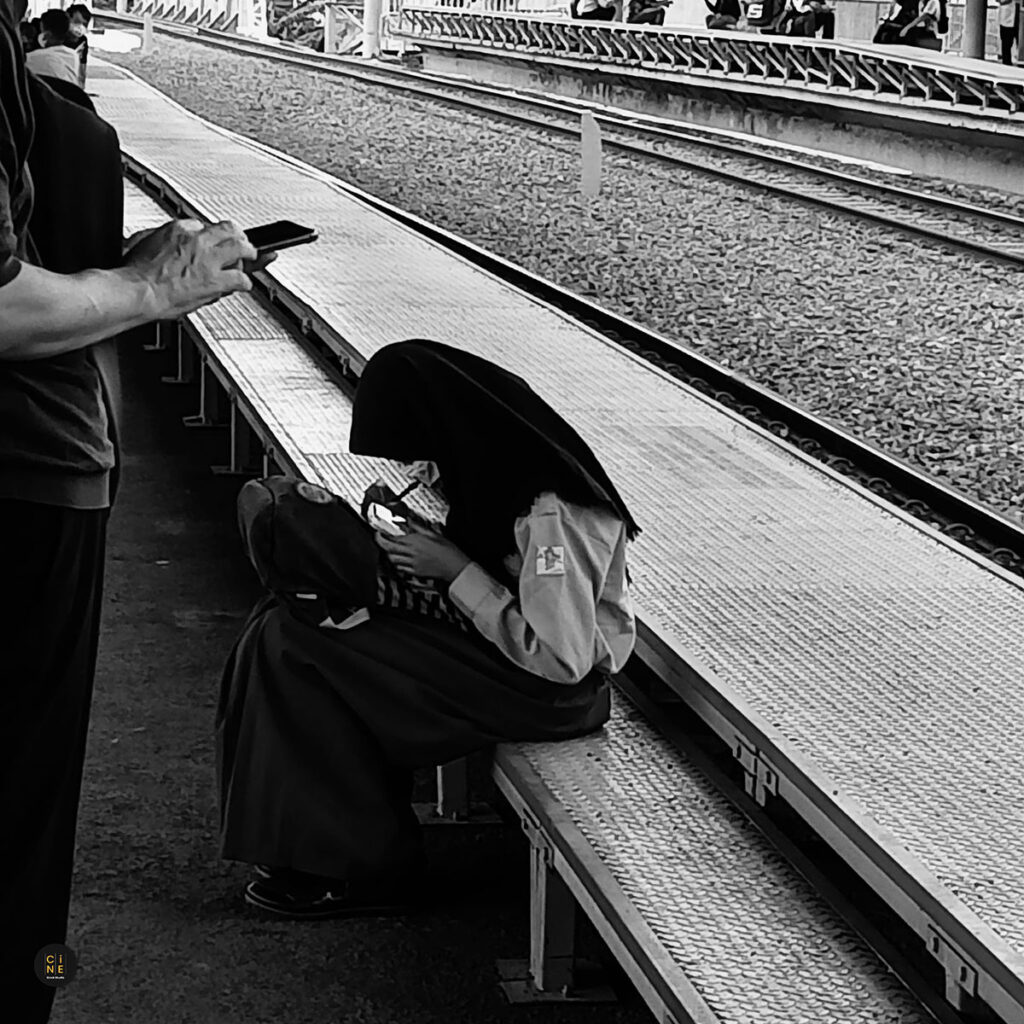 A female student sitting quietly on a station platform edge with her bag during the morning commute.