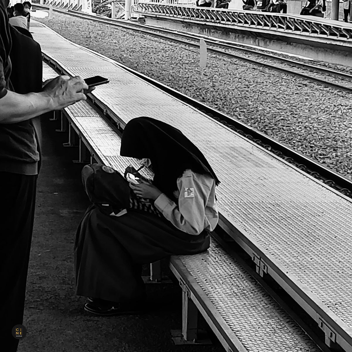 A female student sitting quietly on a station platform edge with her bag during the morning commute.