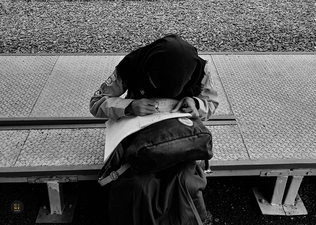 A student bending over her backpack to write on a paper while sitting on the platform structure.