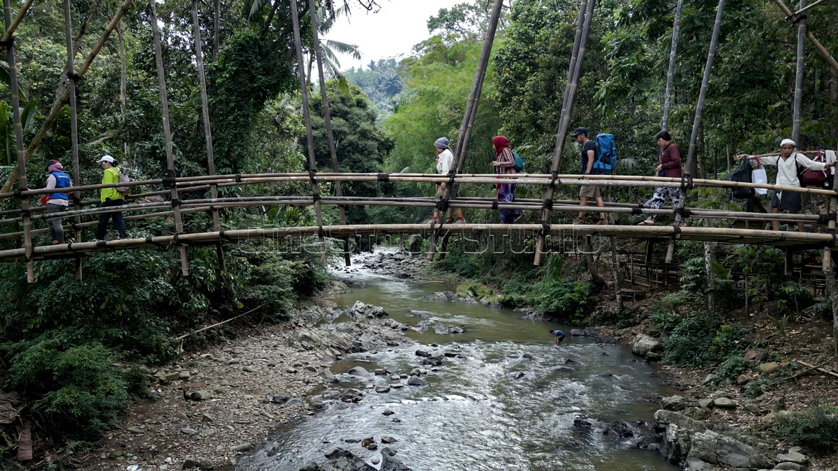 A group of tourists crossing the Gajeboh Bamboo Bridge accompanied by Baduy guides.