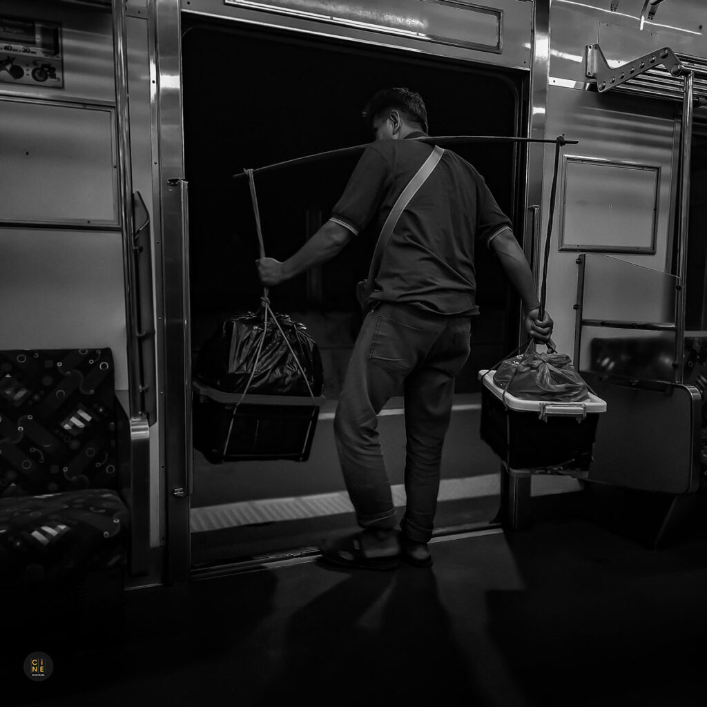 Seorang pedagang tradisional yang membawa barang-barang memasuki gerbong kereta komuter.