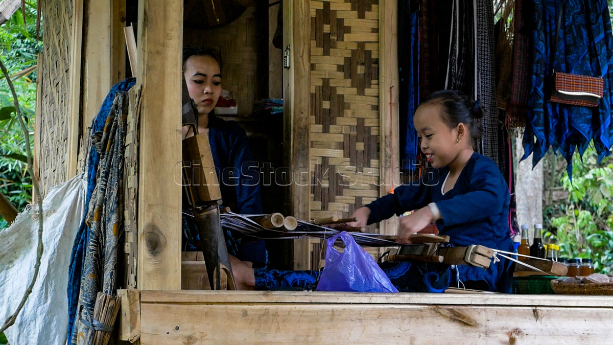 Two generations of Baduy women working together on a wooden house terrace