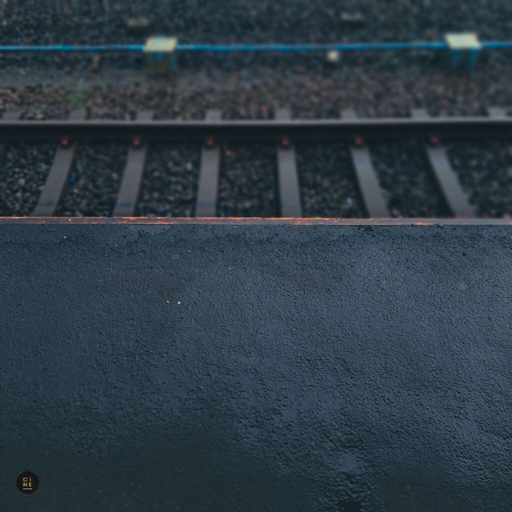 A close-up horizontal shot of wet railway tracks and concrete platform edges glistening under dim evening light.