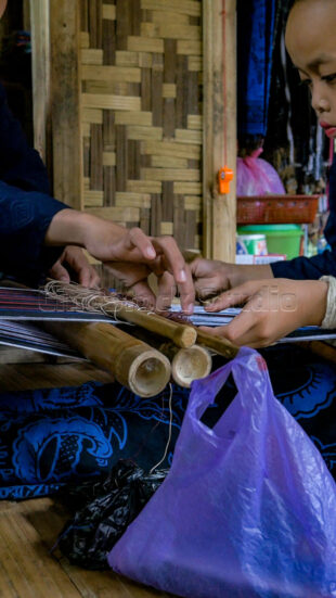Focusing on the small hands that will carry the future of Baduy's textile traditions. Close-up of a child's hands working on a traditional bamboo weaving tool
