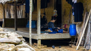 Showcasing the authentic environment of the Baduy community and their open-air workspace. A weaver working in a semi-outdoor area of a traditional bamboo house
