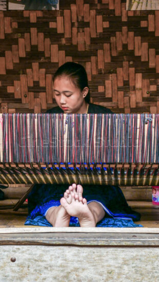 A portrait of dedication, showing the deep concentration required for authentic handmade textiles. Vertical shot of a young Baduy woman focused on her weaving work