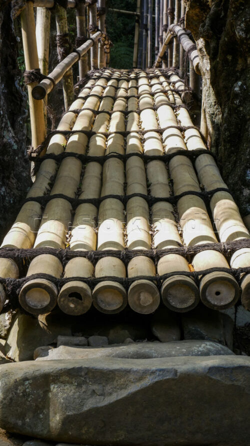 The worn and polished texture of the bamboo planks, shaped by years of footsteps from locals and travelers. Vertical perspective shot of the bamboo walking surface of the bridge.