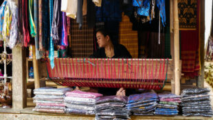 Rows of completed "Tenun Baduy" showing the rich colors and traditional patterns. Stacked finished woven fabrics ready for sale at a village terrace