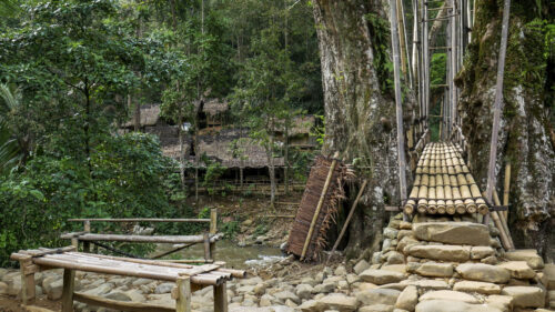 Natural engineering: large river stones used as a solid and stable foundation for the bamboo bridge structure. Close-up of the river stone foundation at the base of the bridge.