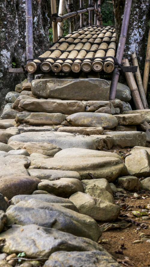 Every step is part of the tradition; these stone stairs mark the beginning of the crossing toward Inner Baduy. Vertical shot of the hand-laid stone steps leading up to the bridge.