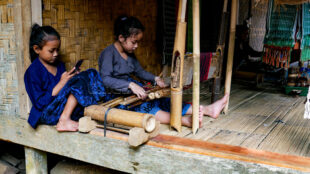 The early education of Baduy children as they observe and practice traditional weaving techniques. Two young Baduy girls sitting on a terrace learning to use a loom